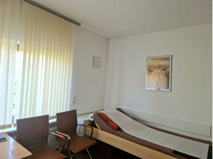 Behandlungsraum der Praxis Brenner mit Liege, Stühlen und großem Fenster